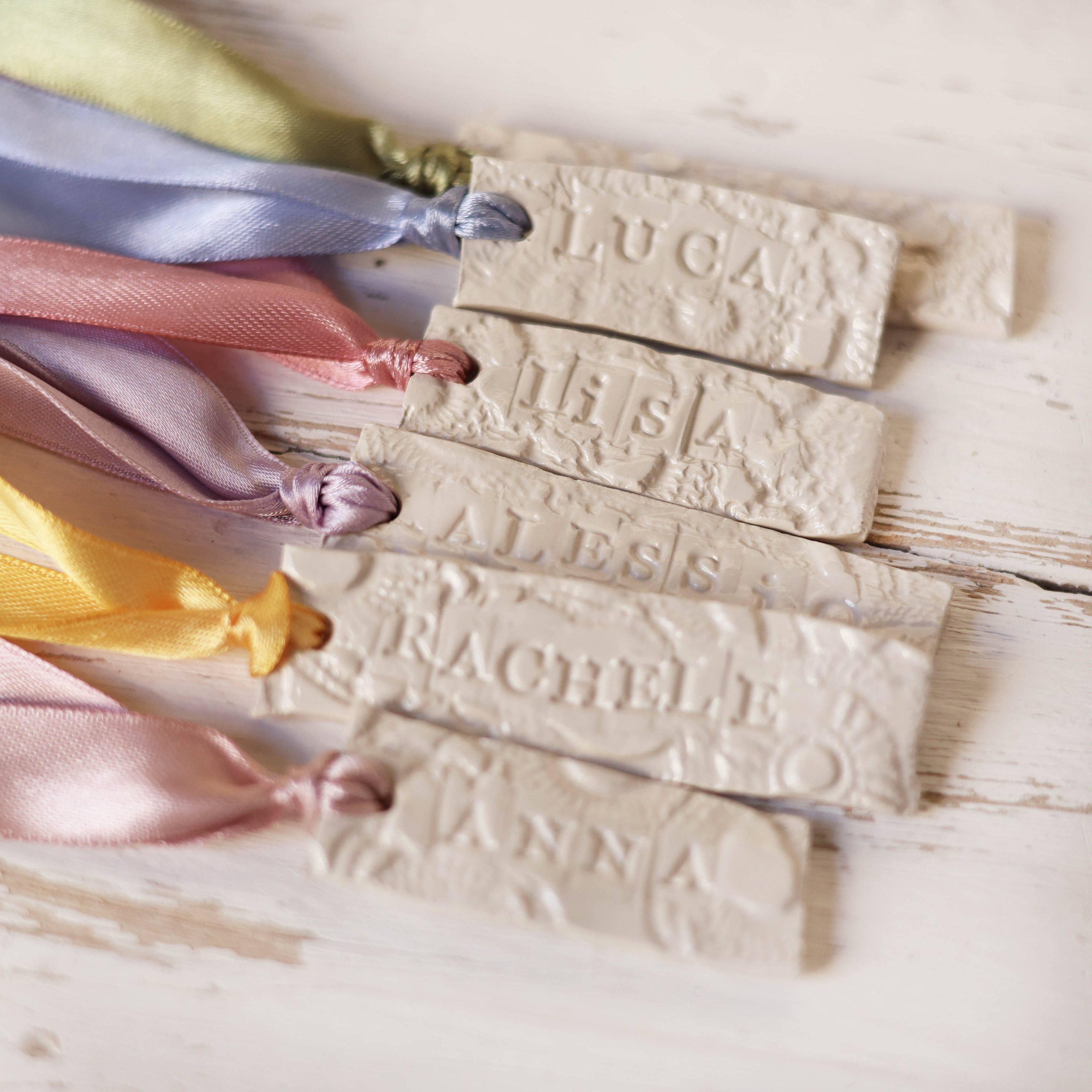 Segnaposto artigianale di ceramica con nomi invitati incisi nell'argilla e con nastrini colorati, segnaposto per matrimonio, battesimo e comunione